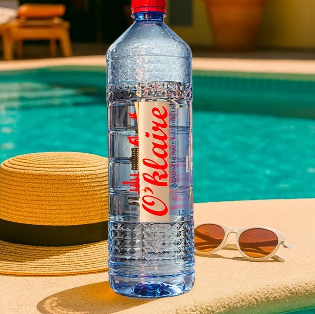 Grande bouteille O'klaire au bord d'un bassin, chapeau de paille et lunettes de soleil à côté